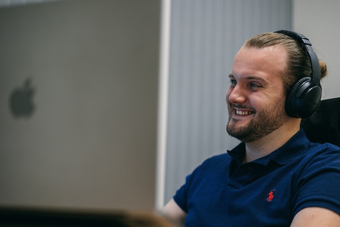 Christoph Harrison bei der Arbeit am Mac, mit Kopfhörern und einem Lächeln