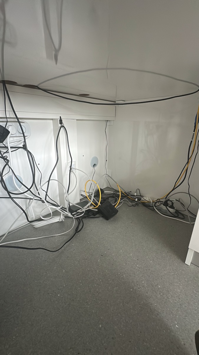Vorher: unter der Anmeldung. Netzteile, Verlängerungen und Netzwerkkabel lagen lose am Boden.