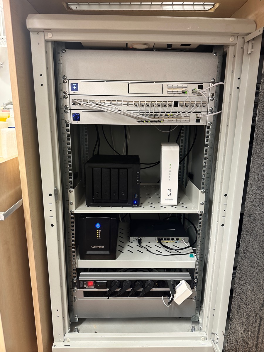 Nachher: der zweite Standort. UniFi Dream Machine Pro, ein UniFi Switch statt drei verschiedener, Synology NAS, und die USV steht im Schrank statt offen im Empfangsbereich.
